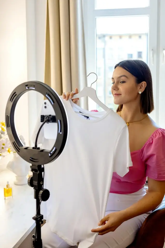Services Woman influencer showcasing a white shirt in a video recording setup.
